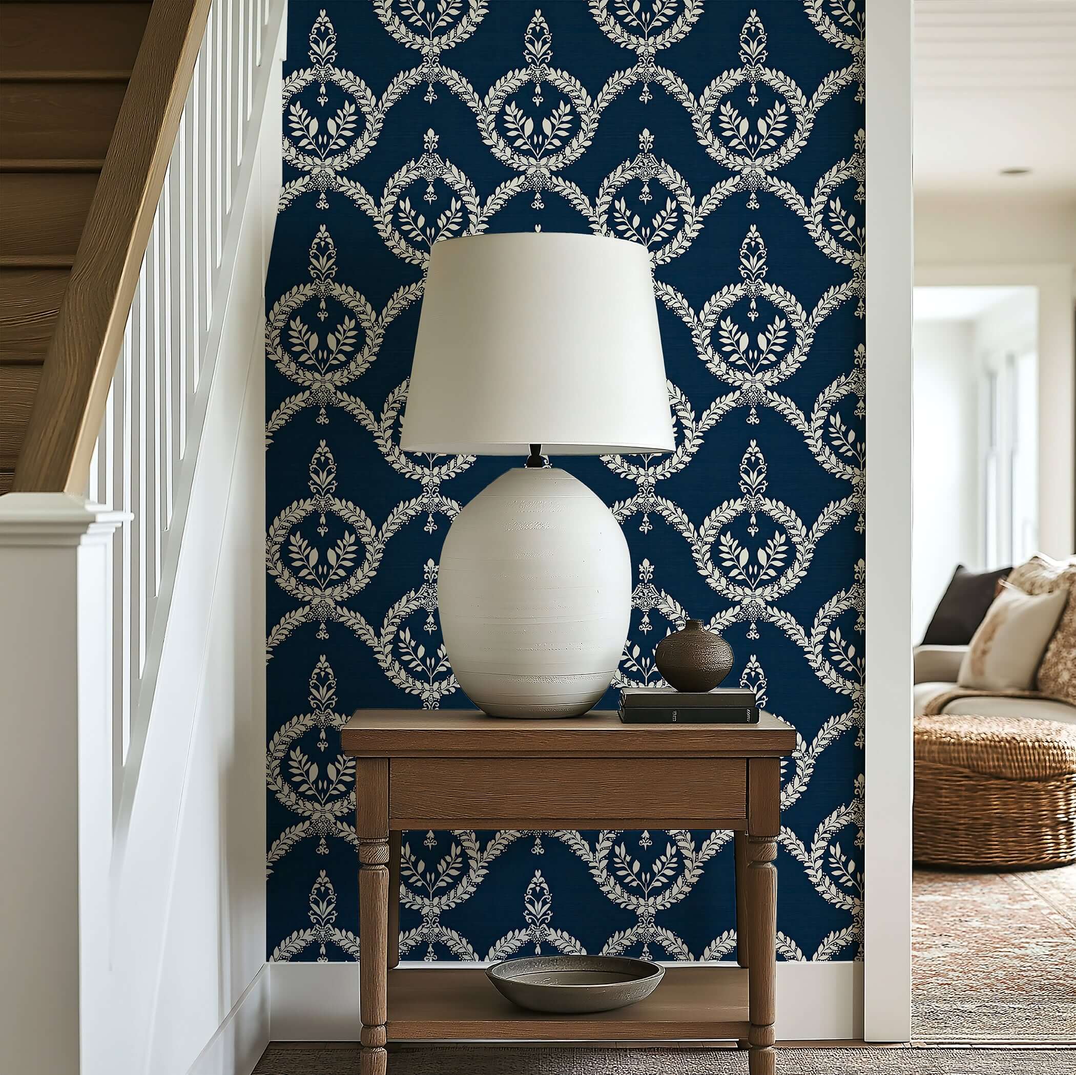 Dark navy wallpaper with ivory laurel wreath patterns, enhancing an elegant and traditional look in a hallway with a lamp and table.