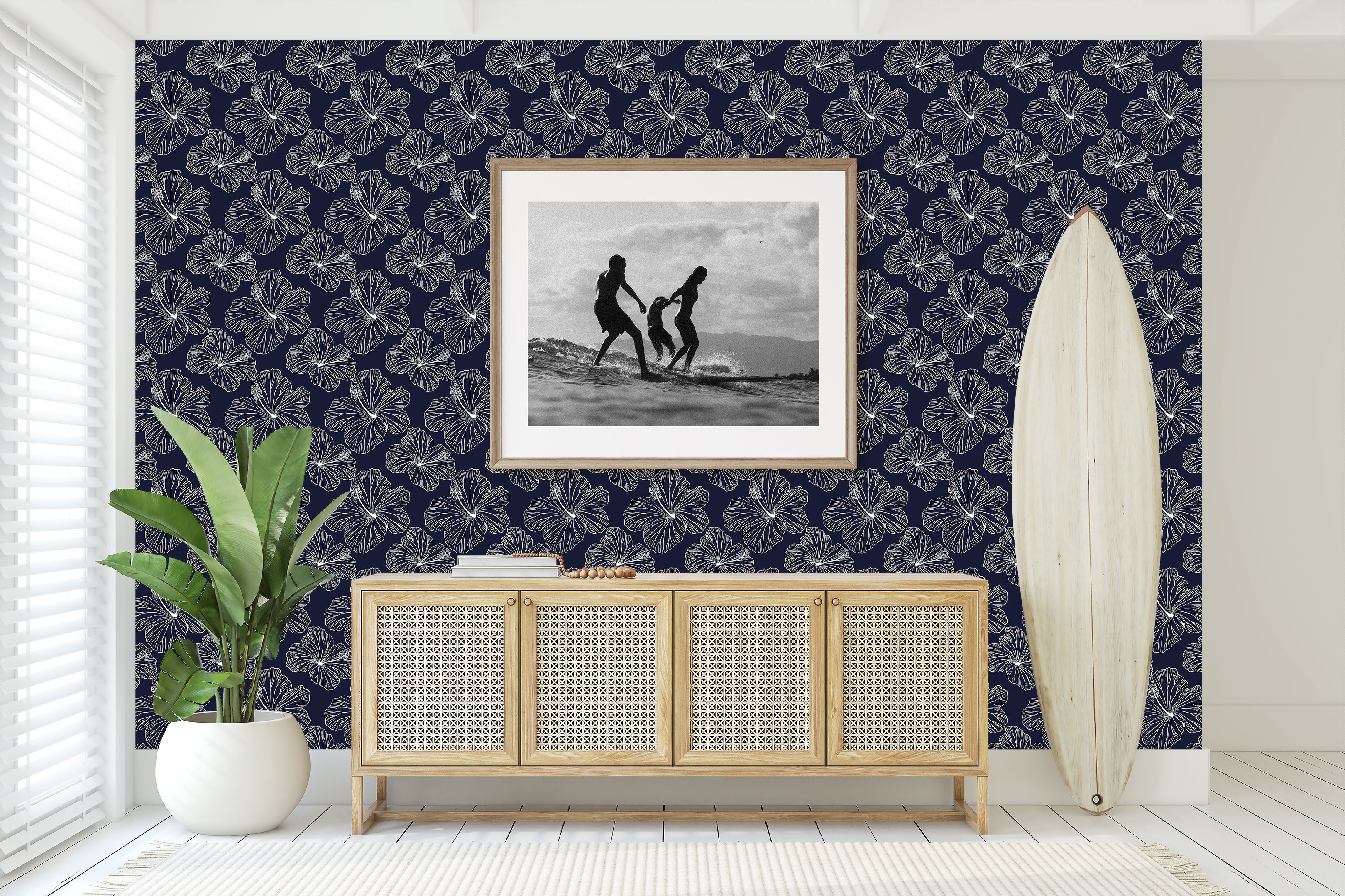 Island Nights Floral Wallpaper with hibiscus on navy background, enhancing a coastal living room setting with surfboard and plant decor.