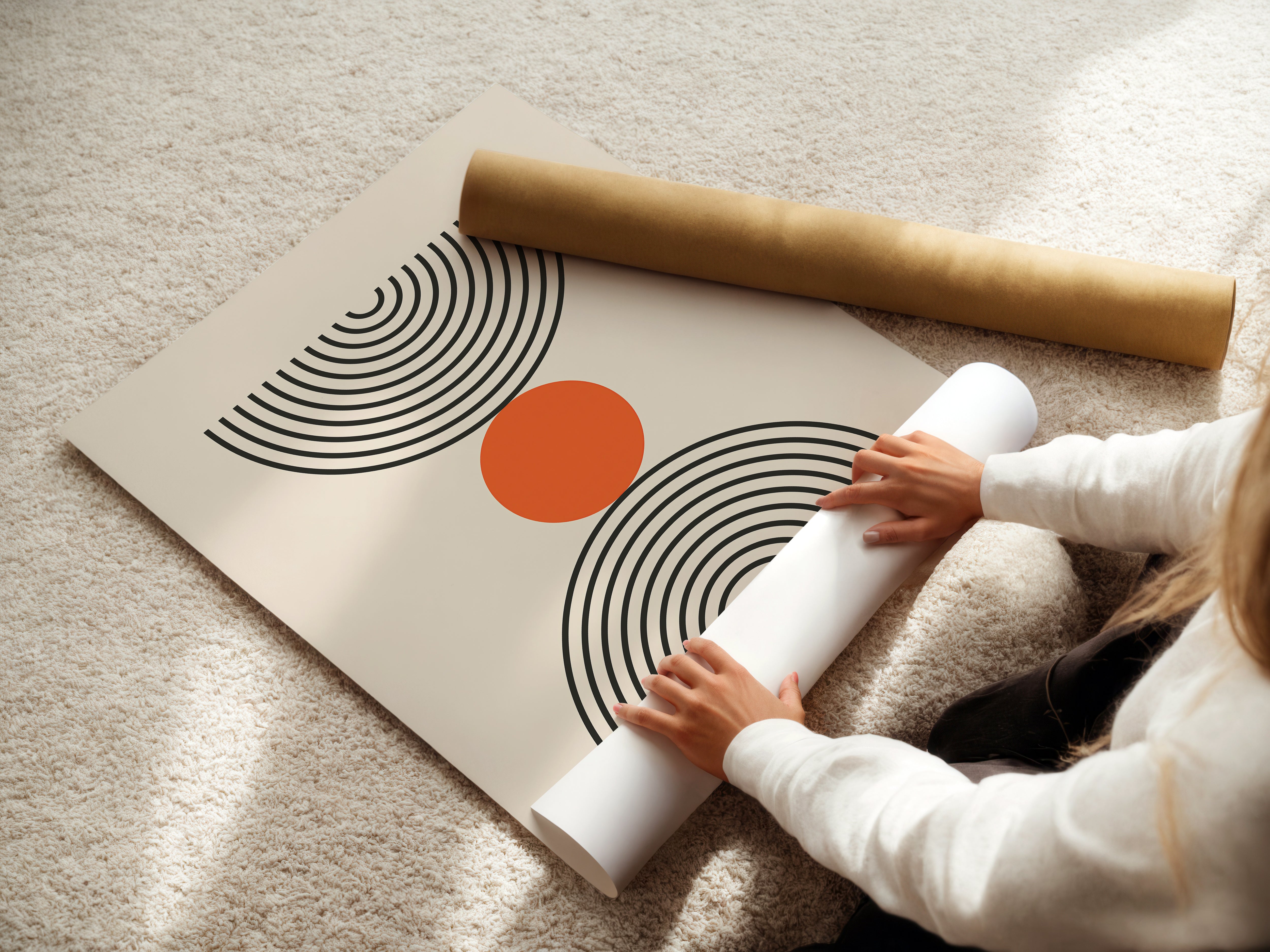 Person rolling up a Bauhaus-inspired wall art print with concentric semicircles and a burnt-orange circle.