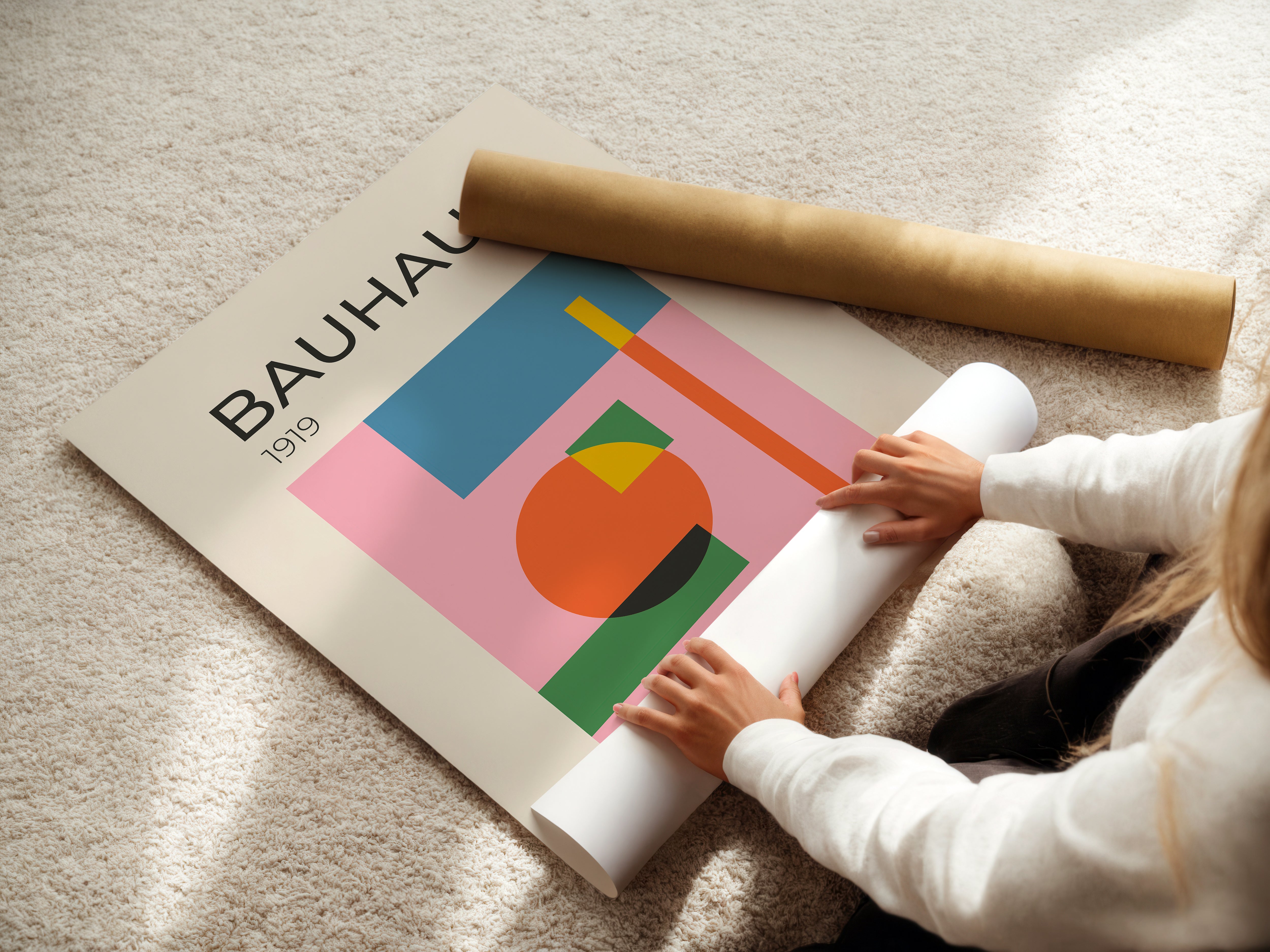 Person unrolling a Bauhaus-inspired art print featuring abstract shapes and vibrant colors on a light carpet.