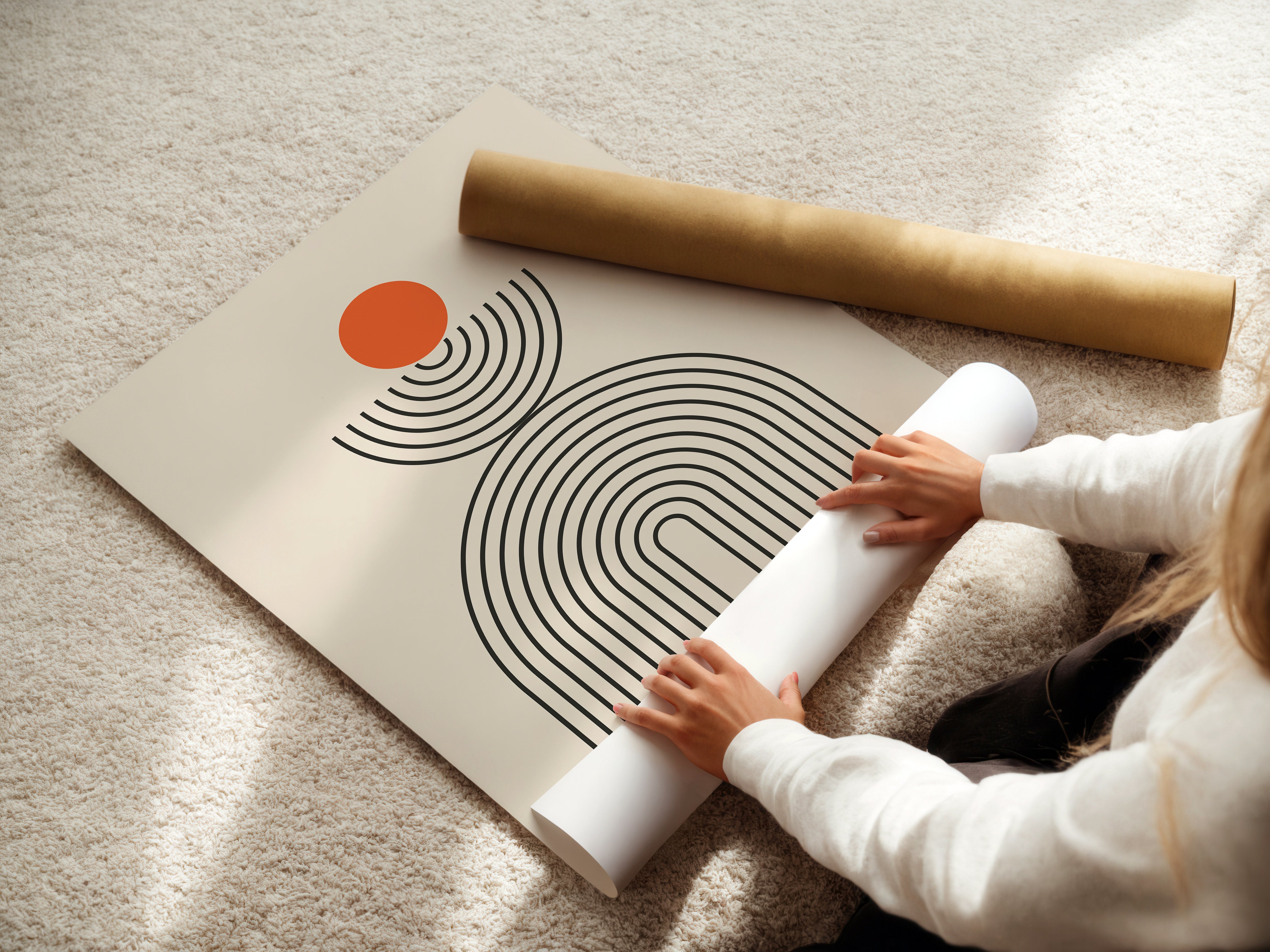 Person unrolling a Bauhaus-inspired art print with orange circle and linear designs on a textured surface.