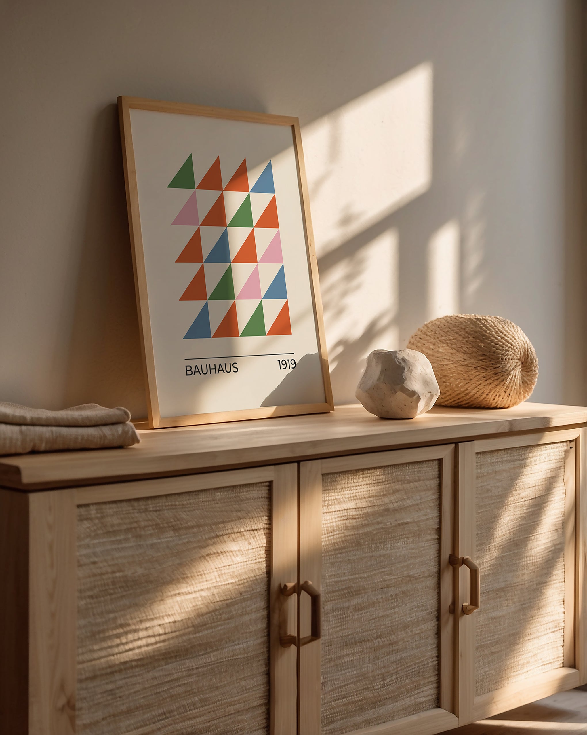 Bauhaus wall art with colorful triangles, displayed on a wooden console in a sunlit modern interior.