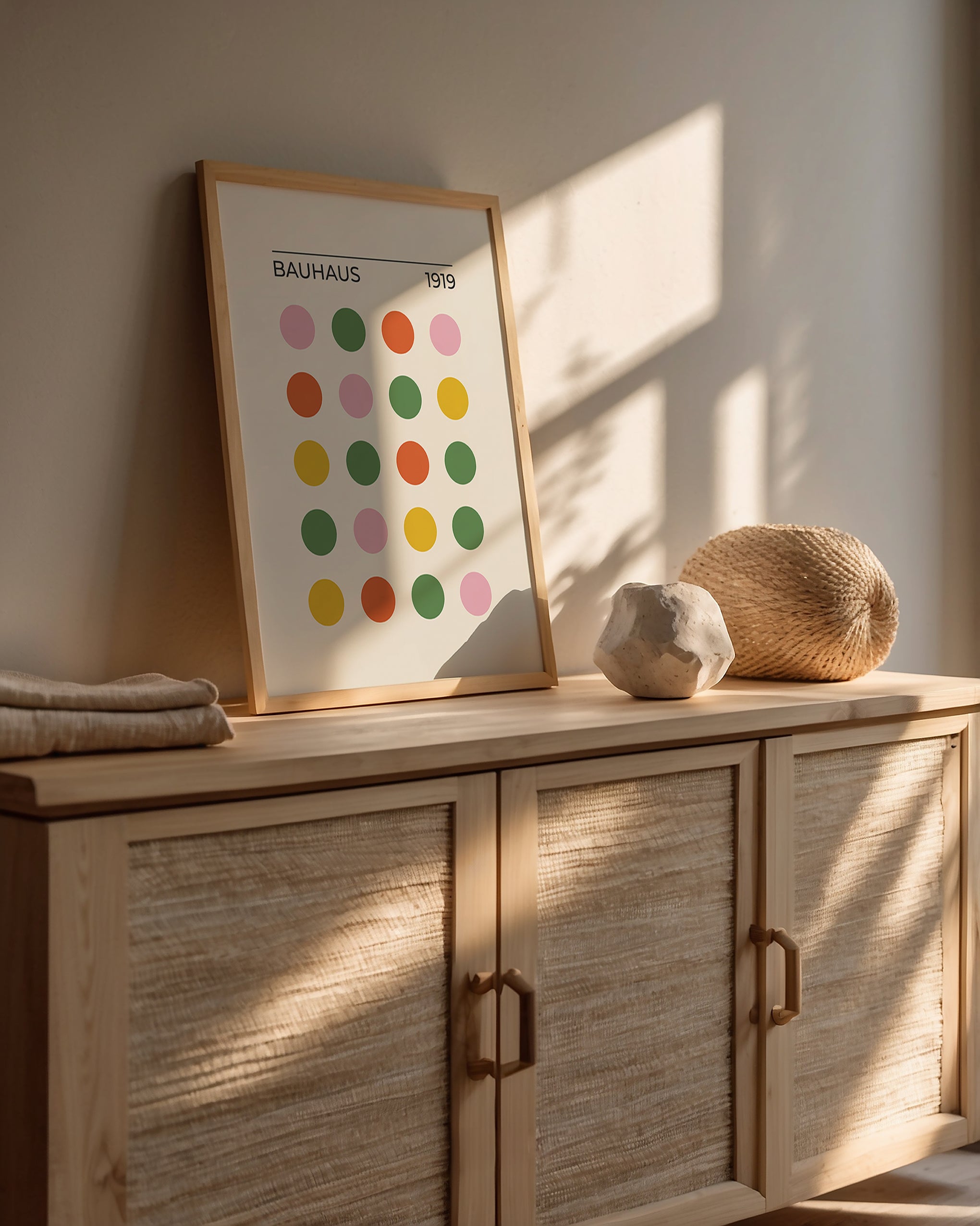 Bauhaus modern art print with colorful dots on wall above natural wood cabinet and textured decor, showcasing minimalist design.