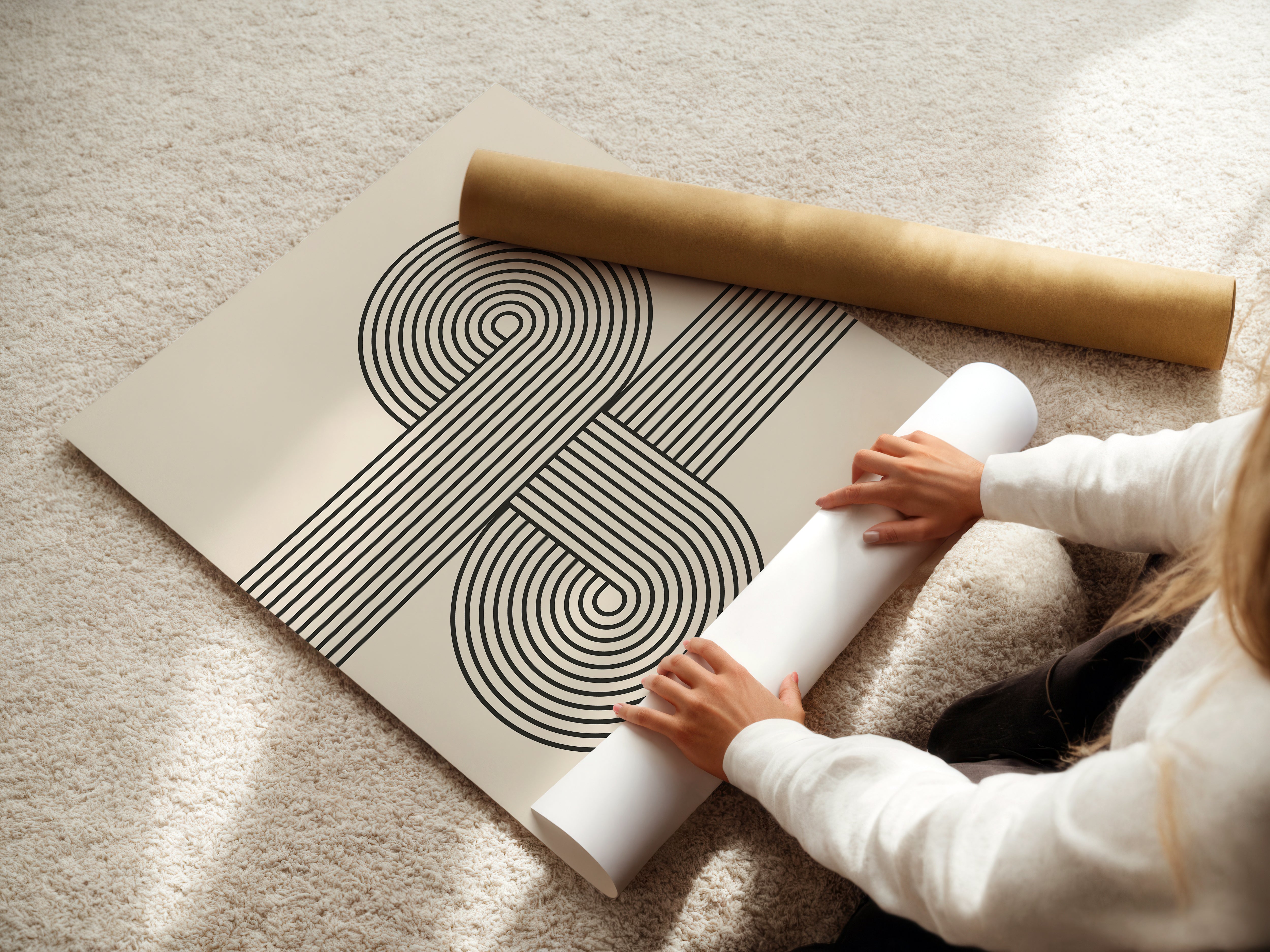Person unrolling a minimalist Bauhaus abstract wall art print with curved lines on a soft carpet.