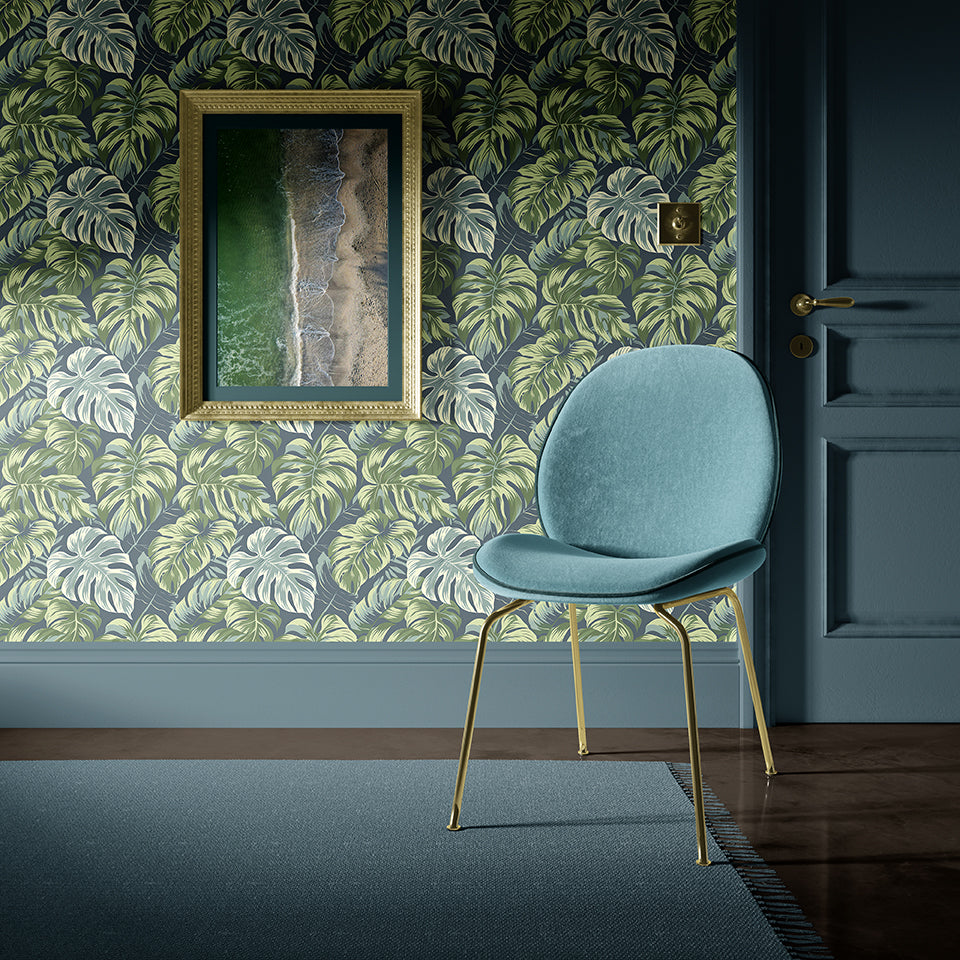 Interior view featuring Tropical Canopy wallpaper with monstera leaves, a stylish chair, and coastal art, enhancing natural décor.