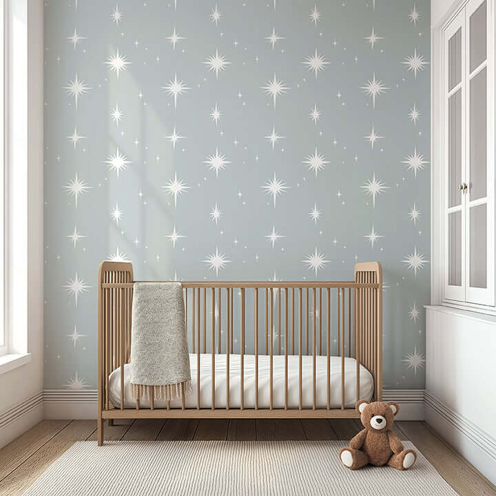 Serene nursery with Dreamy Night Sky wallpaper featuring white starburst stars on gray background, wooden crib and teddy bear.
