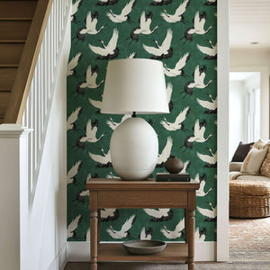 "Flight of the Cranes" wallpaper with white cranes on a forest green backdrop, complementing a classic lamp and wooden table in a cozy space.