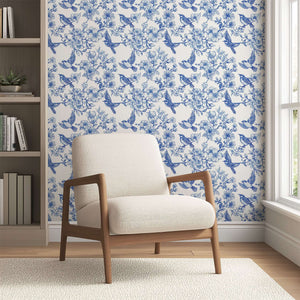 Elegant blue-and-white songbird toile wallpaper in a serene living room with a modern armchair.