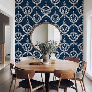Navy wallpaper with ivory laurel wreath pattern behind a dining table, creating a vintage crest look for elegant interiors.