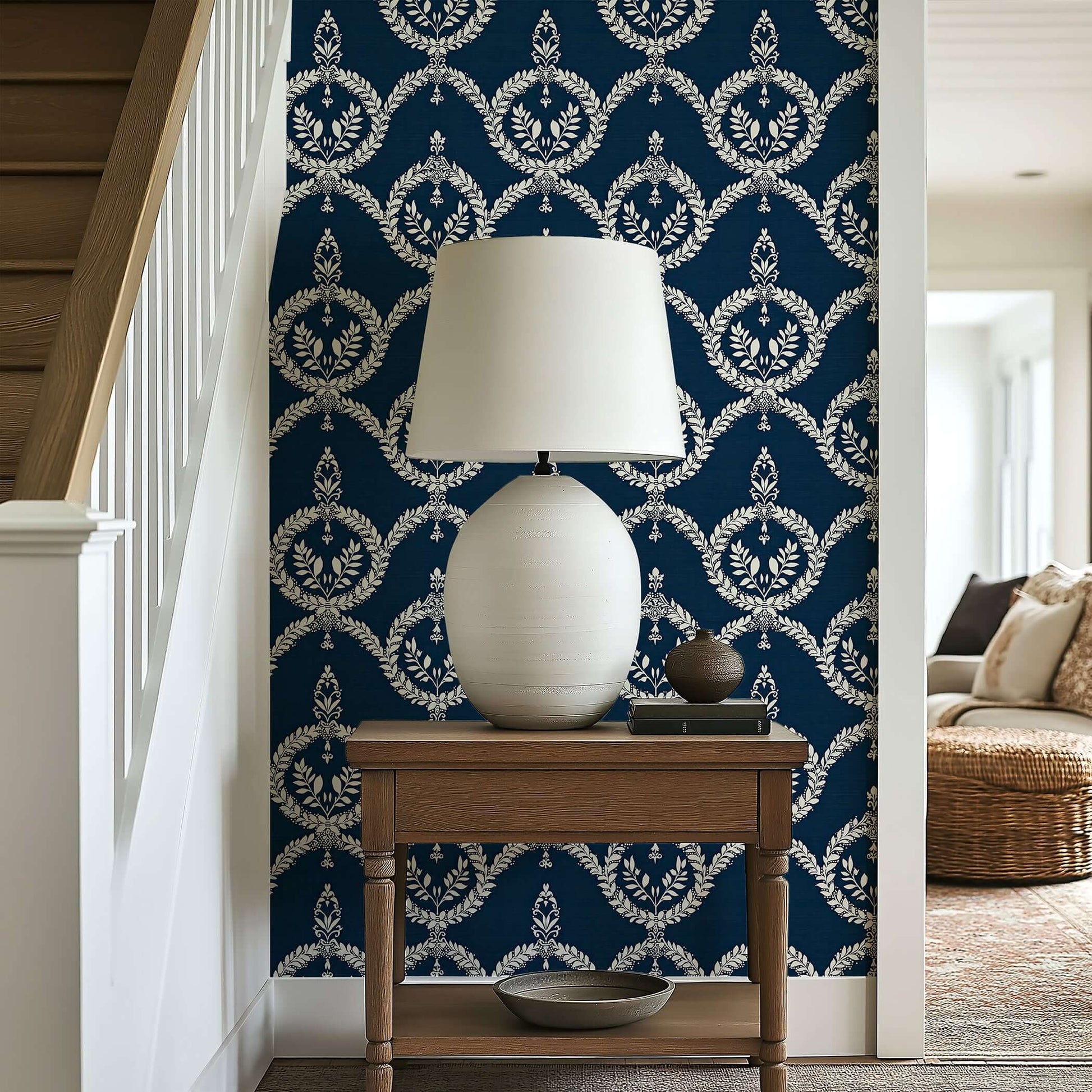 Dark navy wallpaper with ivory laurel wreath patterns, enhancing an elegant and traditional look in a hallway with a lamp and table.