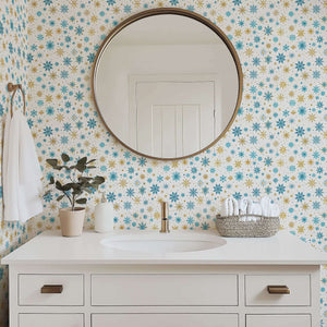 Mid-century modern bathroom with Golden Snowfall wallpaper featuring gold and blue snowflakes, round mirror, and white sink vanity.