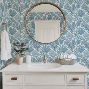 Bathroom with Maritime Meadow wallpaper featuring coastal blue ocean plant motifs, coral design, and elegant mirror above white vanity.