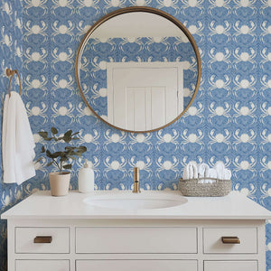 Elegant blue coastal wallpaper featuring white crabs and sea foliage in a bathroom with a round mirror and modern vanity.