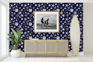 Coastal room with navy wallpaper featuring white seashells and starfish, complemented by beach-themed decor and a surfboard.