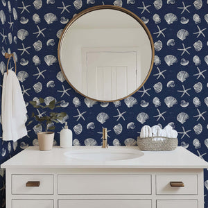 Bathroom with navy coastal wallpaper featuring white starfish and seashells, complementing a round mirror and elegant sink area.