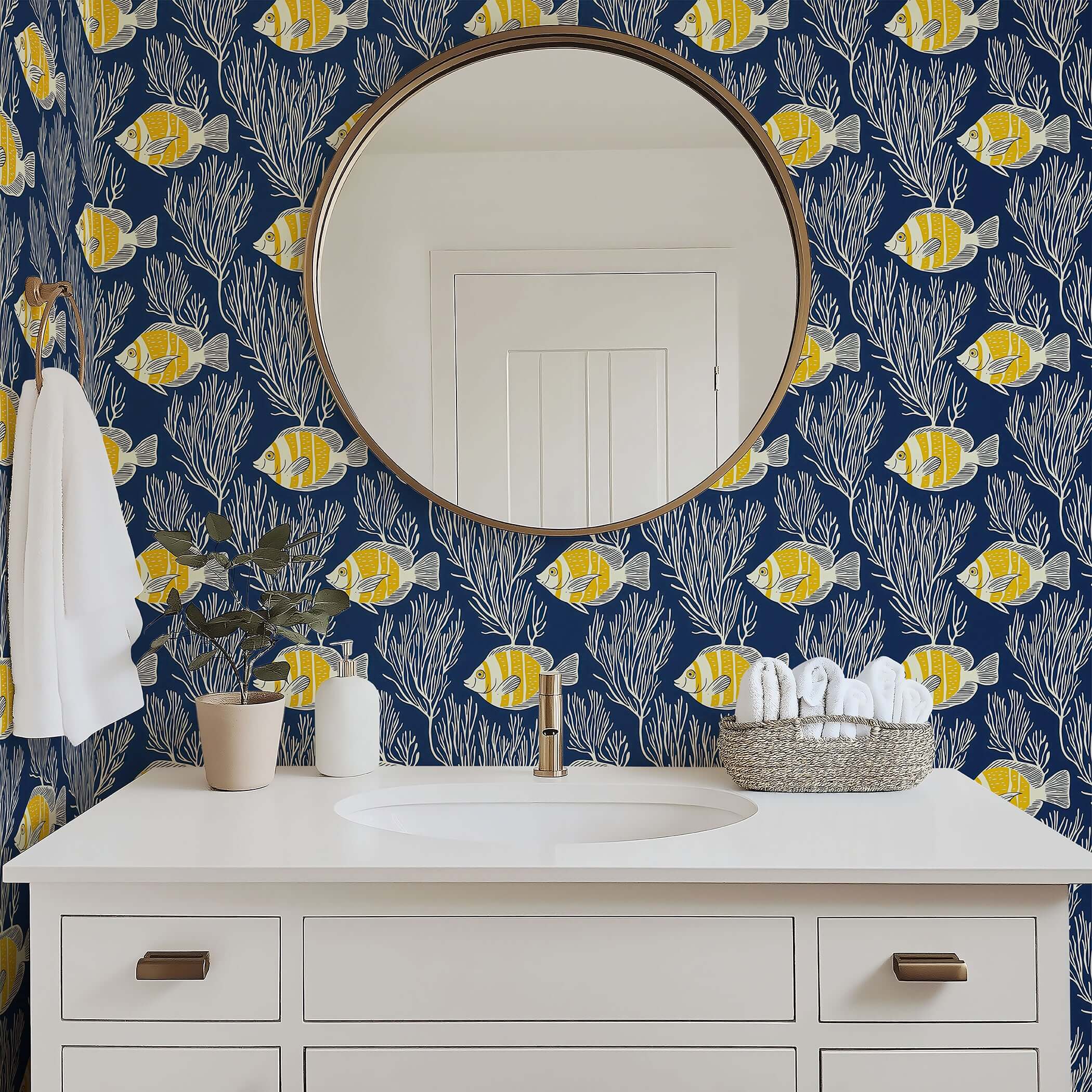 Coastal wallpaper with yellow fish and coral, enhancing ocean aesthetics in a bathroom with a round mirror and white vanity.