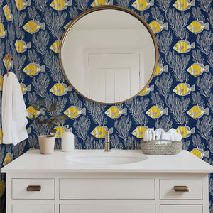 Coastal wallpaper with yellow fish and coral, enhancing ocean aesthetics in a bathroom with a round mirror and white vanity.