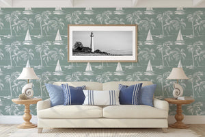 Seafoam green coastal wallpaper with sailboats and palm trees, enhancing a serene nautical-themed living room with a lighthouse artwork.