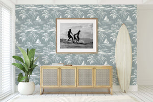 Lagoon Tranquility wallpaper with palm trees and boats in a coastal living room setting, featuring a surfboard and framed art.