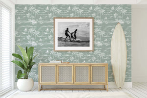 Palm Coastline wallpaper with palm trees and boats in a coastal-themed room, featuring a surfboard and framed photo, enhancing oceanic vibes.