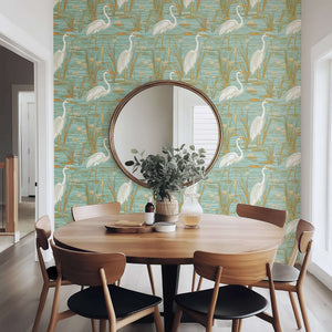 Coastal dining room with 'Tranquil Marshland' wallpaper featuring blue herons, teal, and tan tones for a serene atmosphere.
