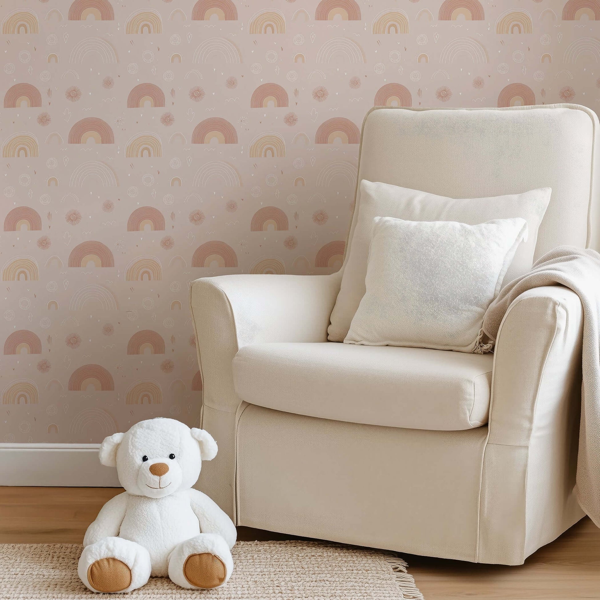 Soft beige wallpaper with hand-drawn pink rainbows in a cozy nursery featuring a teddy bear and cream armchair, perfect for kids' rooms.