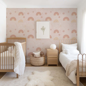 Pastel Rainbow Delight Wallpaper in nursery with cribs, featuring pink hand-drawn rainbows and sunbursts; modern design for kids' rooms.