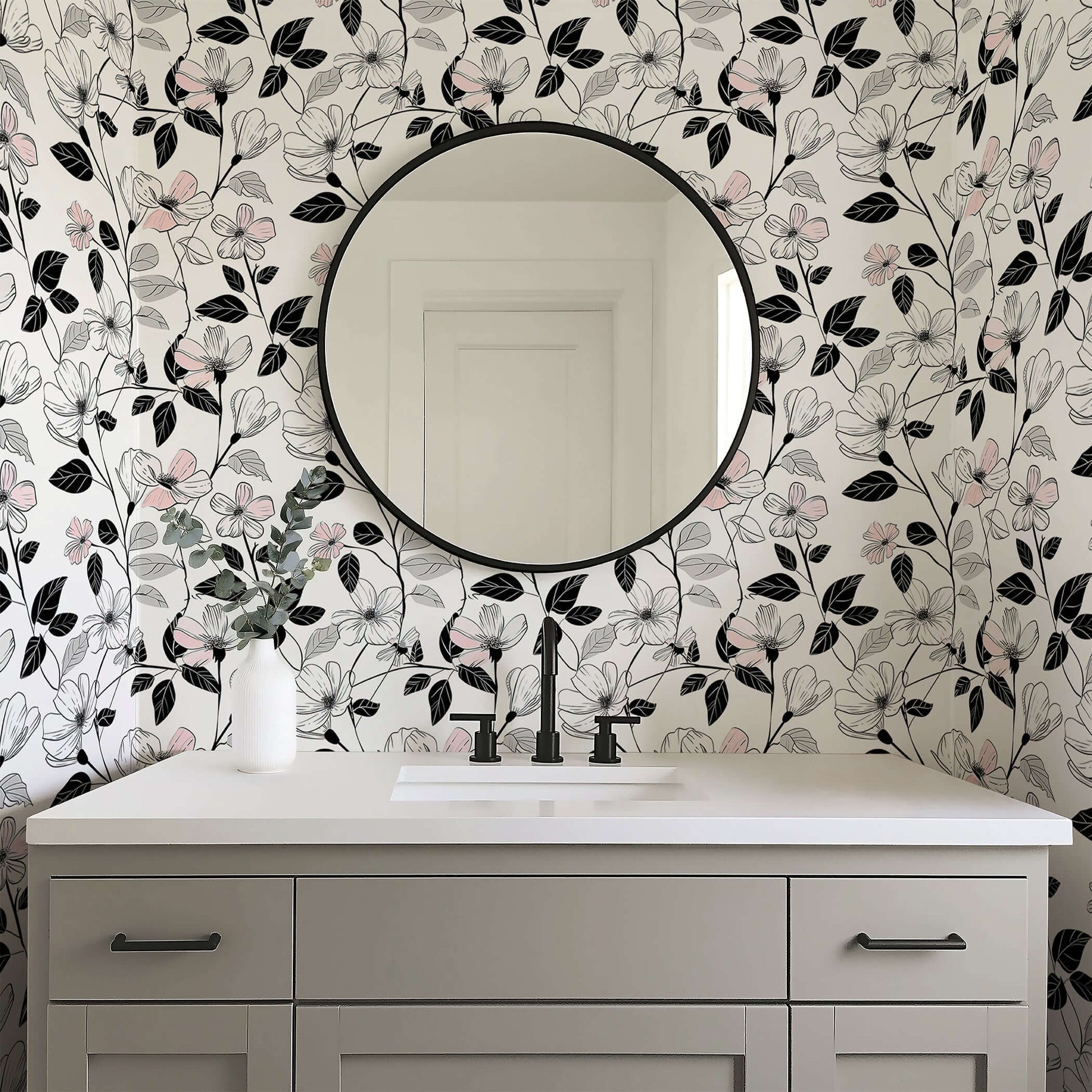 Modern monochrome floral wallpaper with blush flowers and black foliage in a bathroom with a round mirror.