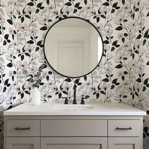Modern monochrome floral wallpaper with blush flowers and black foliage in a bathroom with a round mirror.