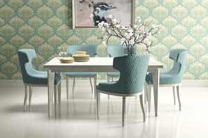 Dining room with teal damask floral wallpaper, modern table, soft blue chairs, and art piece, creating a tranquil and elegant space.