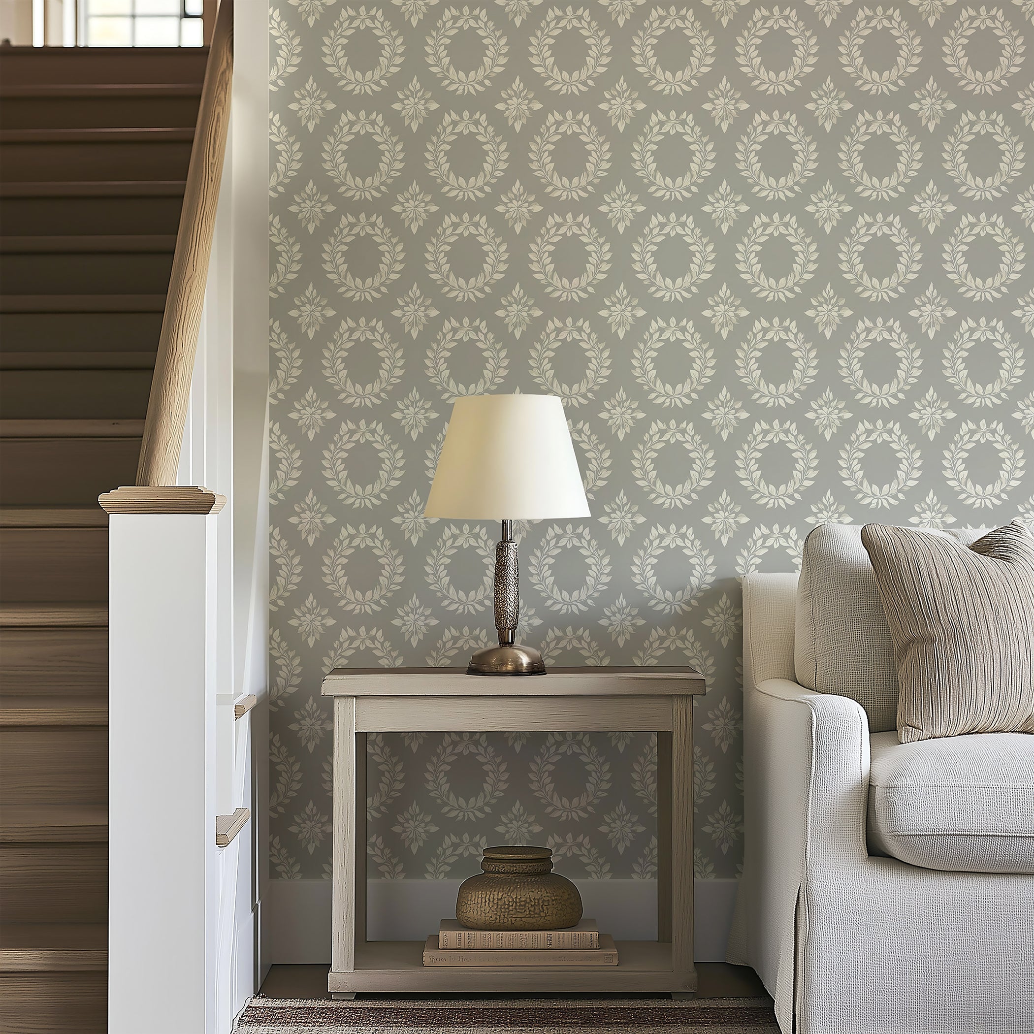 Elegant living room with wall adorned in Timeless Floral Wreaths wallpaper featuring ivory laurel wreaths on a muted sage-gray background.