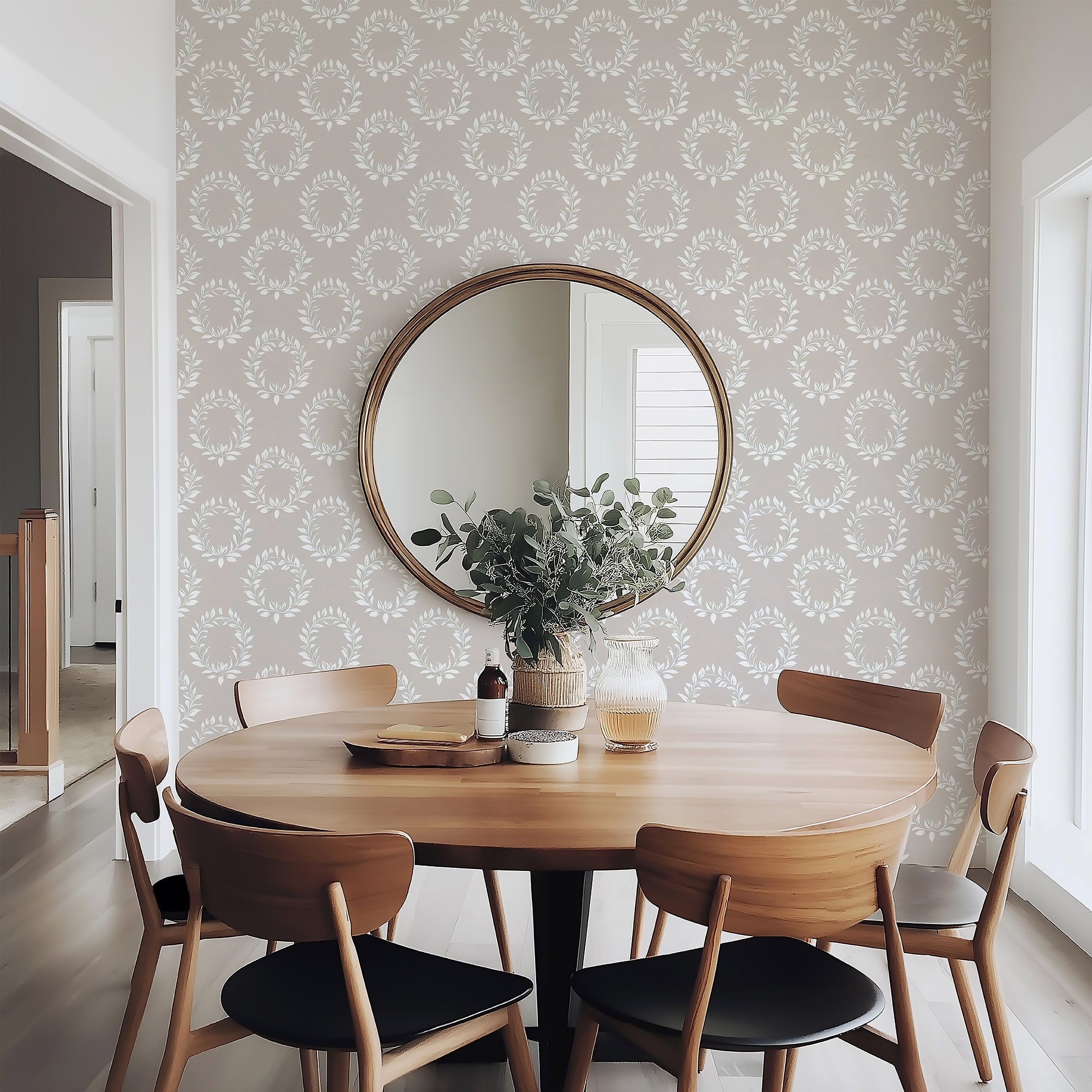 Dining room with Wreath Reverie wallpaper featuring ivory laurel wreaths on a neutral background, complemented by a round mirror and wooden table.