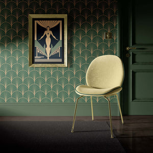 Art Deco geometric wallpaper in gold and emerald green with framed artwork and a beige chair in a sophisticated interior setting.