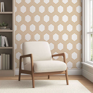 Art Deco geometric wallpaper with bronze hexagons on white background, complementing a modern living room with a beige armchair.
