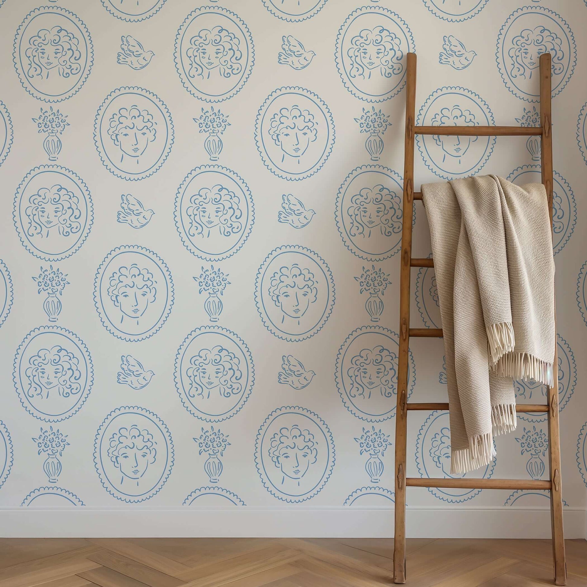 Whimsical blue and white wallpaper with curly-haired portraits, birds, and florals, embodying French vintage elegance.