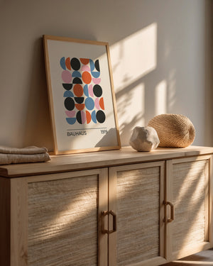 Framed Bauhaus-inspired wall art print on a wooden console with sunlight and decorative elements.