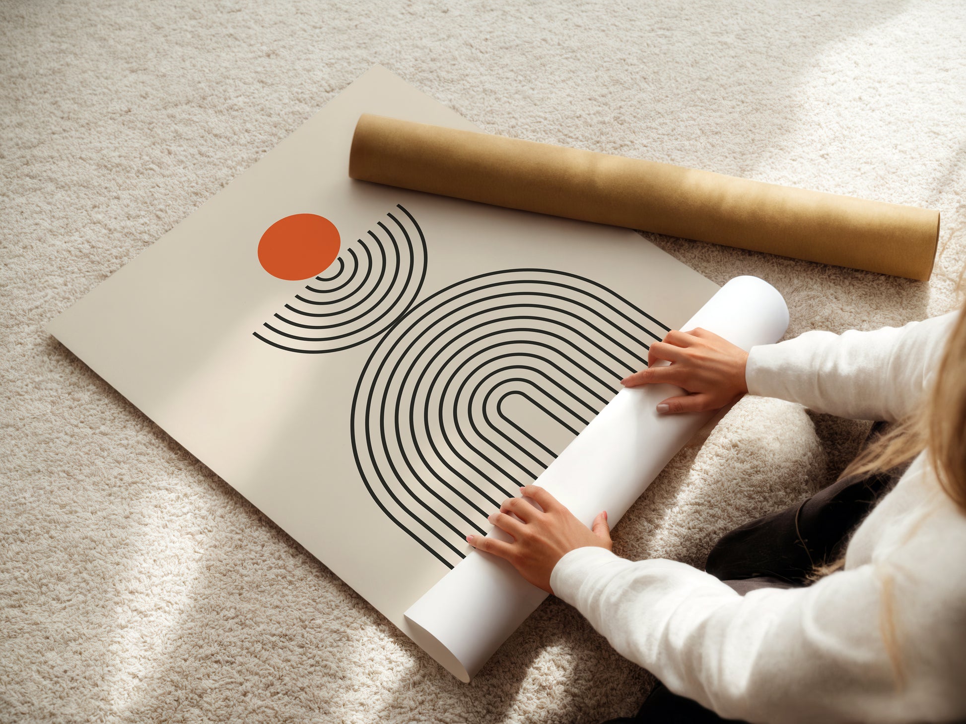 Person unrolling a Bauhaus-inspired art print with orange circle and linear designs on a textured surface.