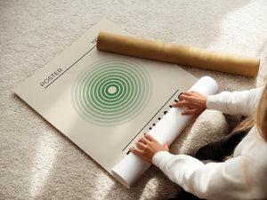 Person unrolling a Bauhaus-inspired minimalist wall art print with concentric green circles on a cozy carpet.