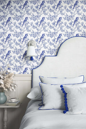 Blue songbird garden toile wallpaper in bedroom, featuring elegant vintage-style French toile design and classic blue birds on branches.