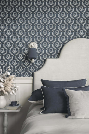 Elegant bedroom with Midnight Laurel wallpaper featuring white laurel wreaths on dark blue, complementing traditional decor.