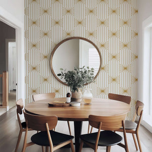 Art Deco wallpaper with gold geometric sunburst lines on ivory background in modern dining room with round mirror and wooden furniture.